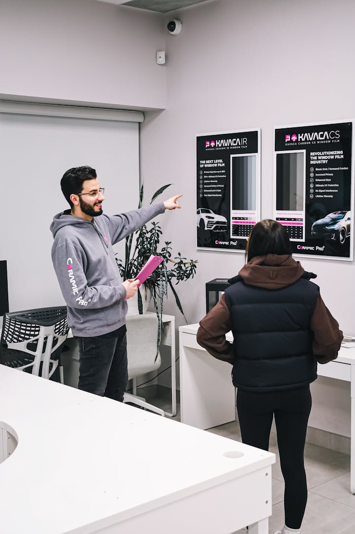 A man assisting a customer in a car showroom with product options.