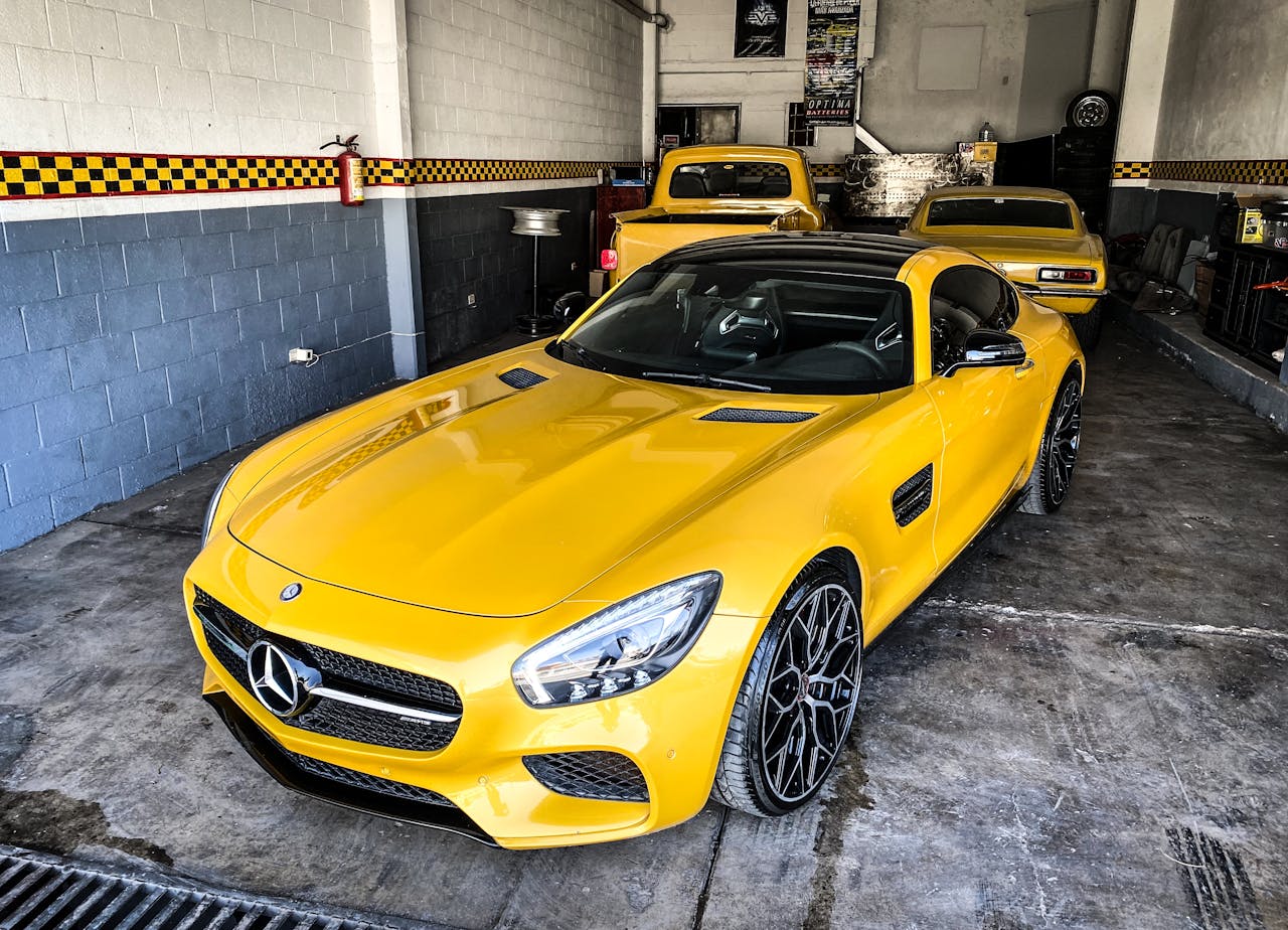 Yellow Mercedes-Benz sports car parked in a garage with other vehicles, exhibiting luxury and style.