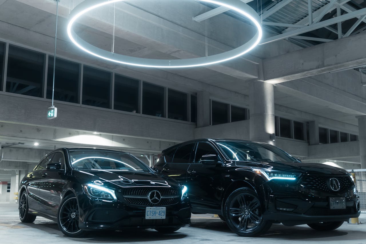 Two luxury cars, a Mercedes and an Acura, parked in an illuminated modern garage.